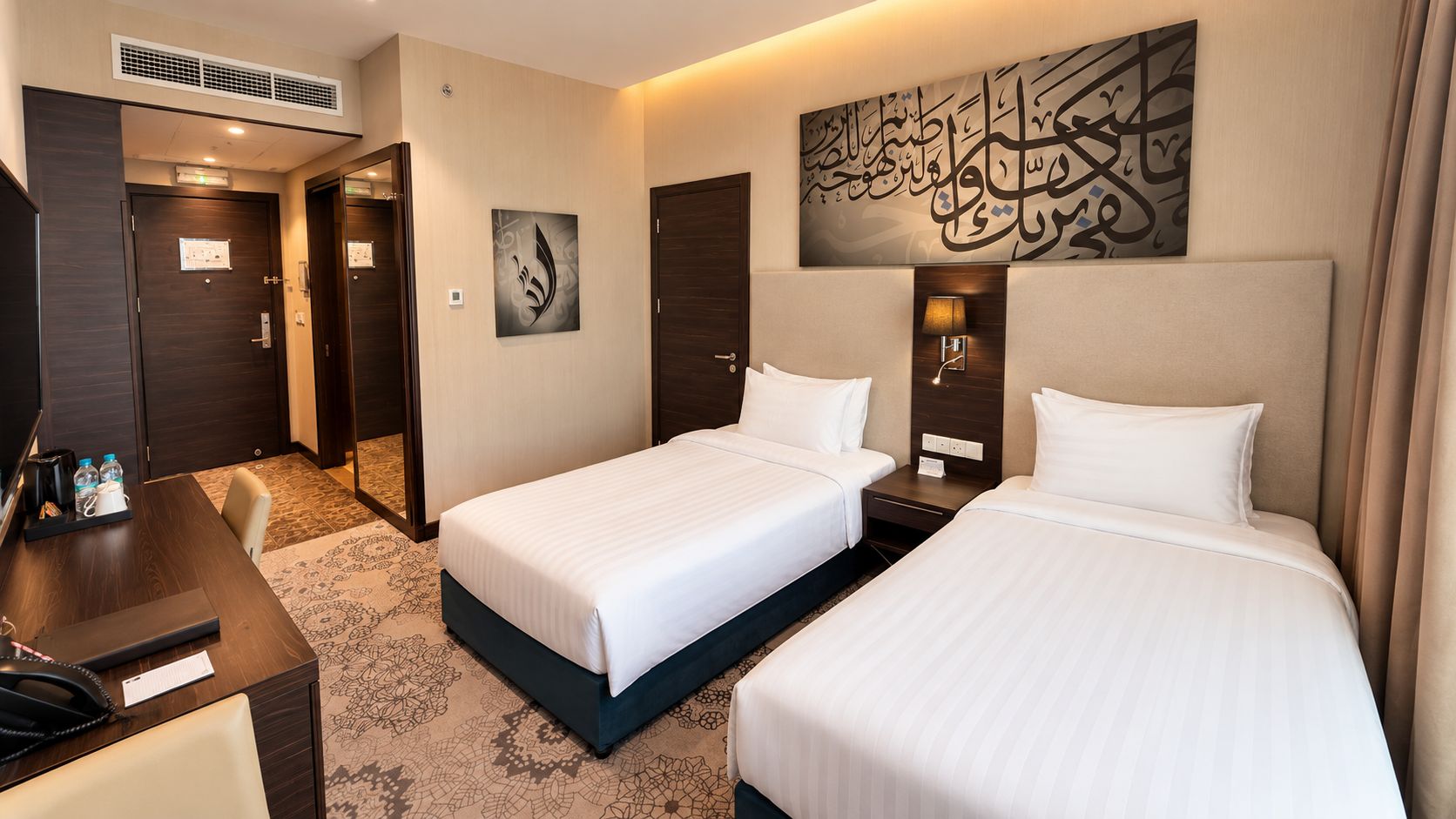 A hotel room with two beds, a desk, a chair, and a large artwork on the wall.