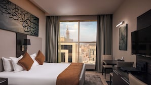 Habitació d'hotel amb un llit gran, escriptori, televisió i vista a un paisatge urbà.