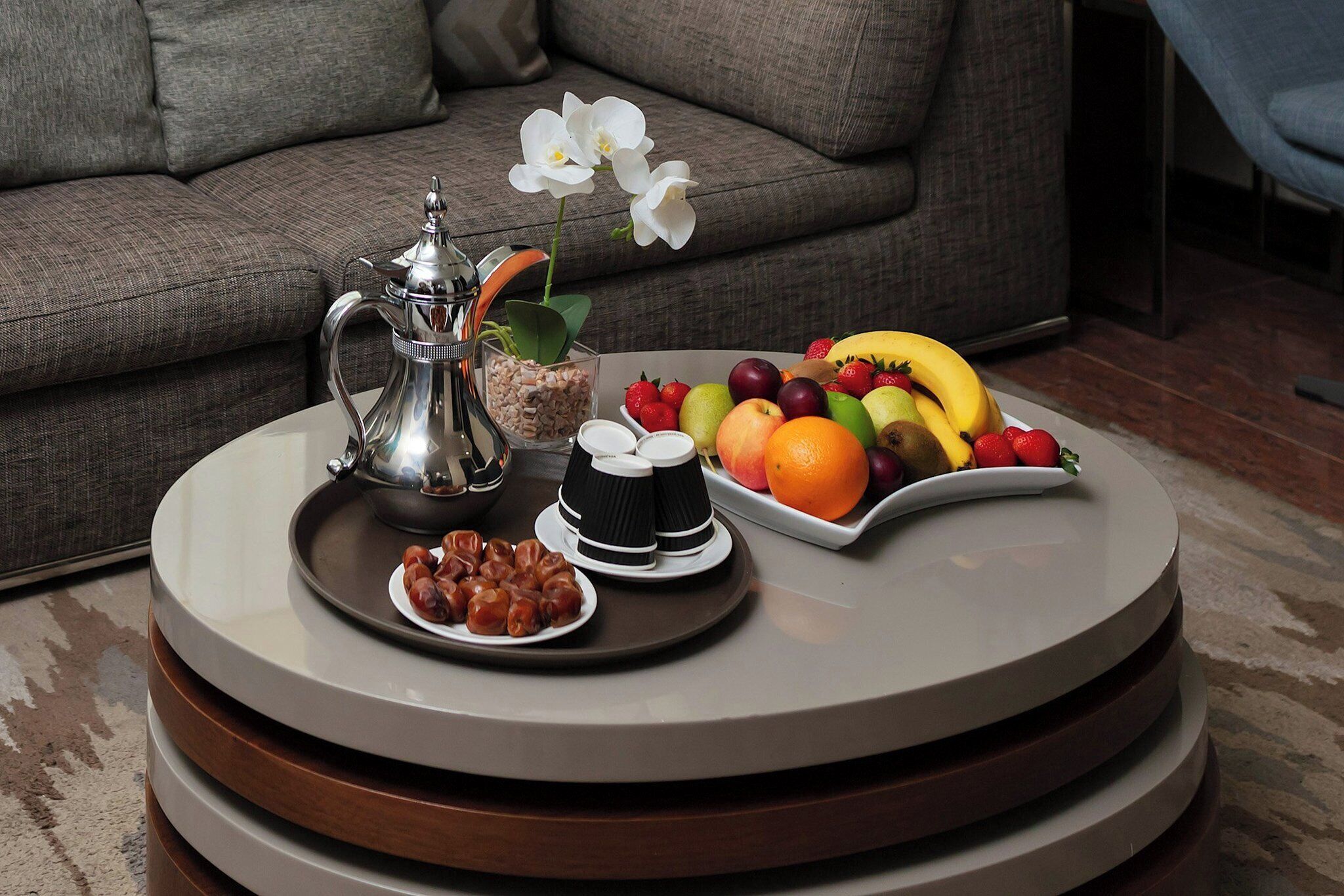 A round table with a tray of food, a coffee pot, and a flower.