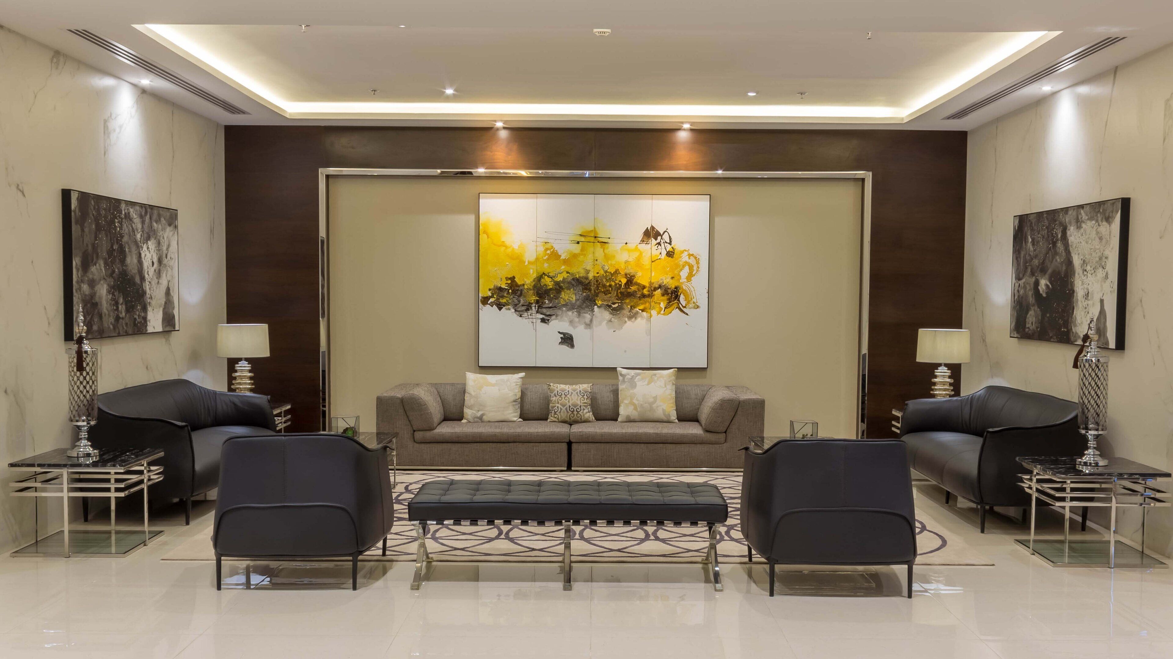 A modern living room with a sofa set, two armchairs, a coffee table, and a large abstract painting on the wall.