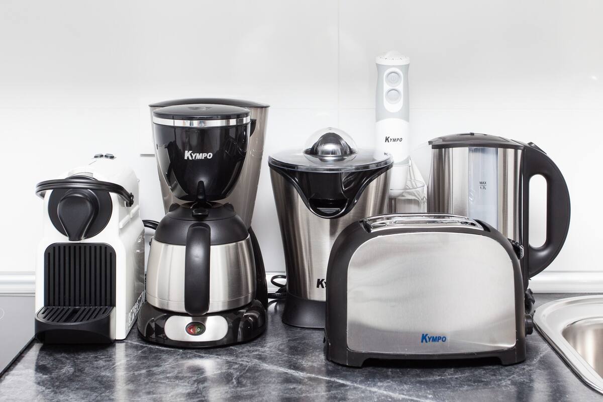 Una cocina con cafetera, tostadora, hervidor y licuadora sobre la encimera.