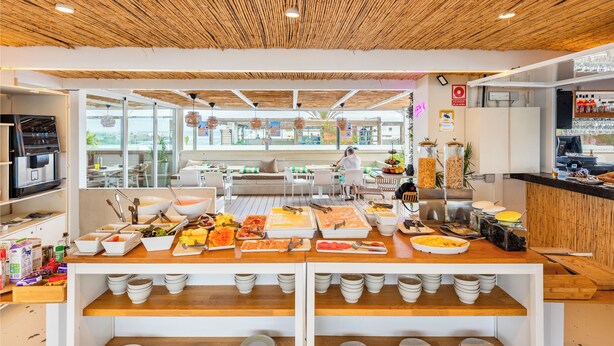 Montaje tipo buffet con diversos alimentos y una zona de estar con vistas al exterior.