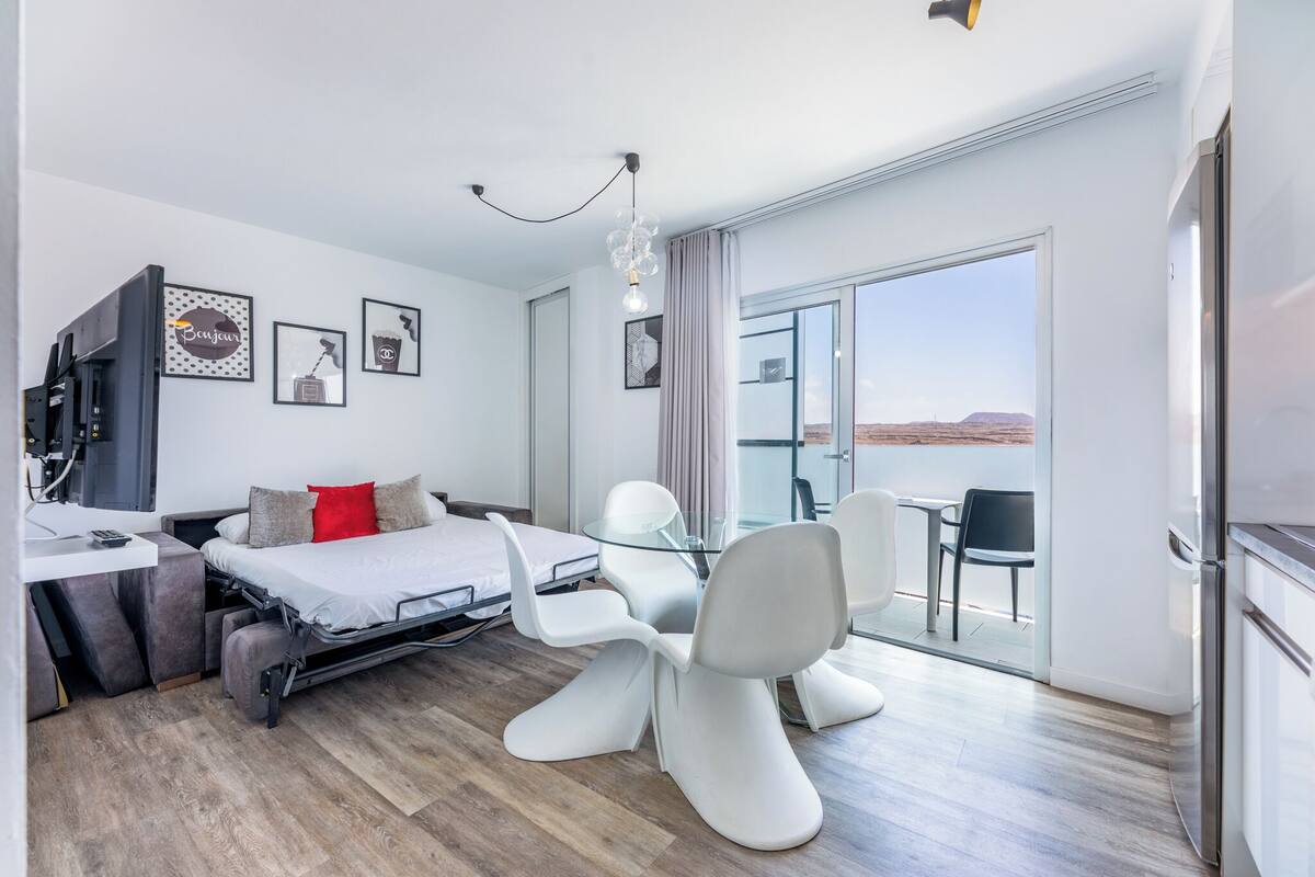 Habitación de hotel moderna con cama, escritorio, silla, balcón y televisor.
