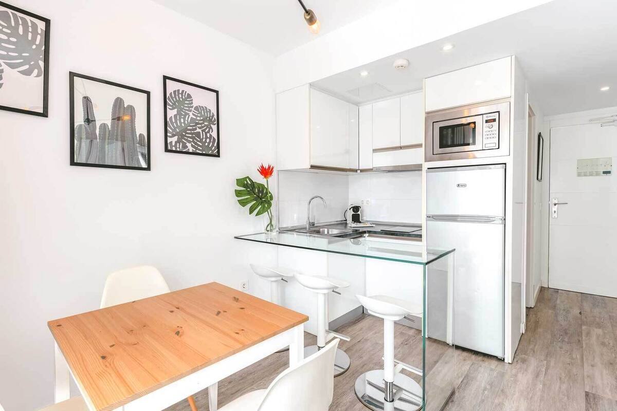 Una cocina moderna con armarios blancos, una isla de cristal y un refrigerador de acero inoxidable.