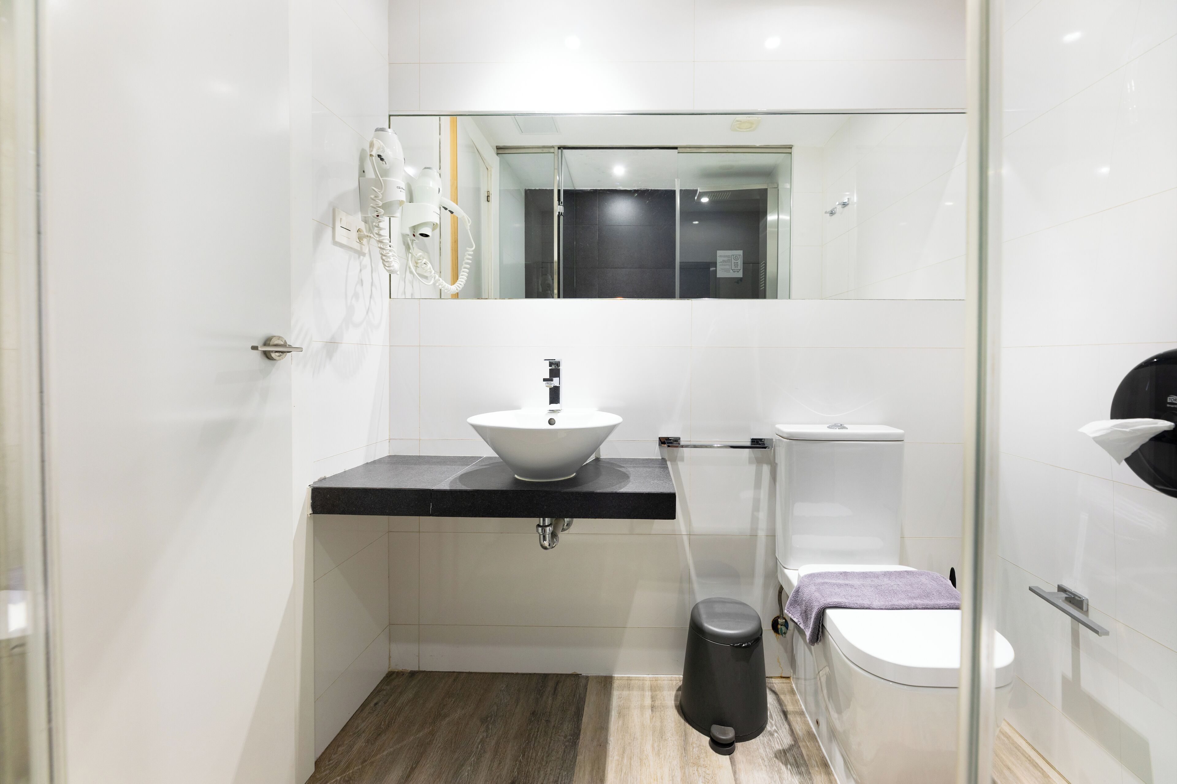 Un baño moderno con lavamanos blanco, encimera negra y cabina de ducha de vidrio.
