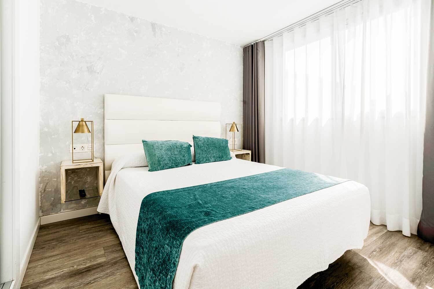 A hotel room with a large bed, two bedside tables, a lamp, and a view of the outdoors.