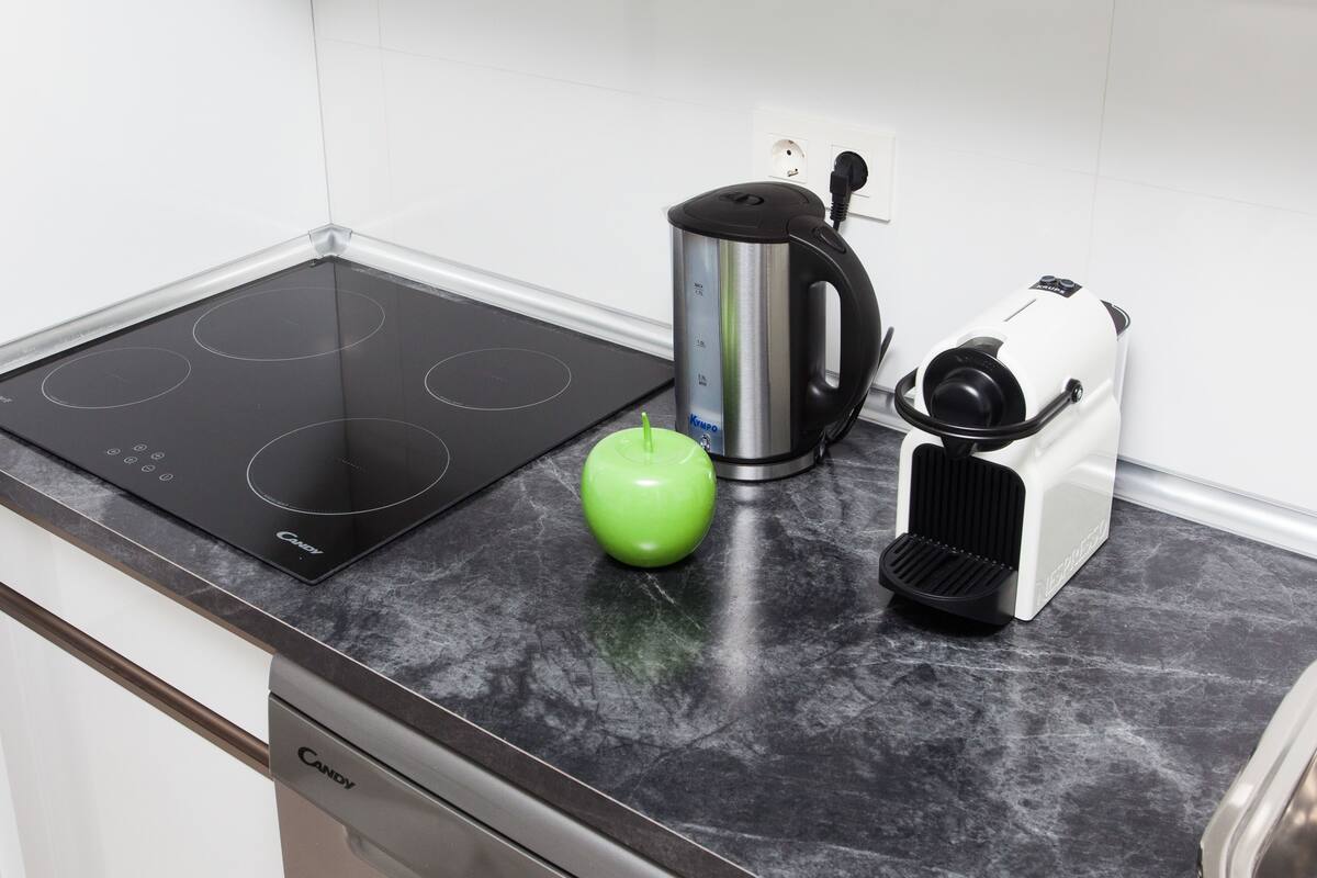 Una cocina con placa de inducción negra, hervidor y tostadora.