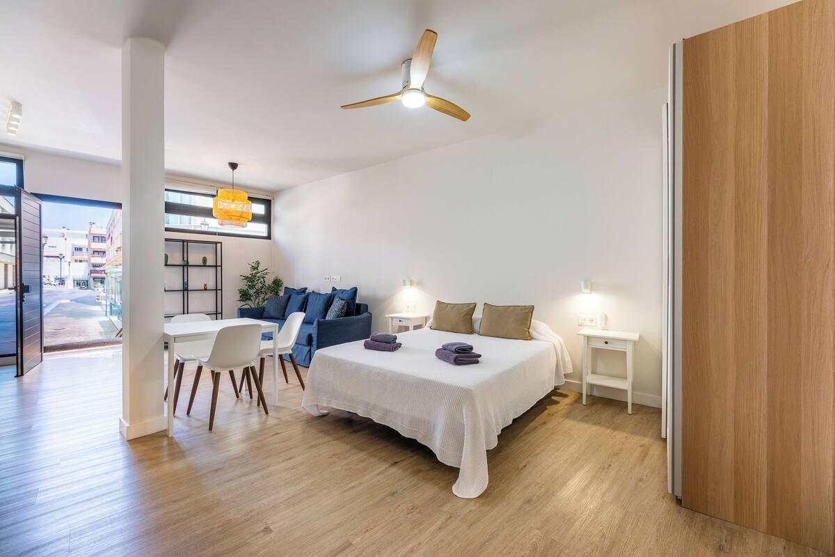 Una habitación de hotel moderna con cama, escritorio, silla, ventilador de techo y vistas al exterior.