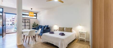 A modern hotel room with a bed, a desk, a chair, a ceiling fan, and a view of the outside.