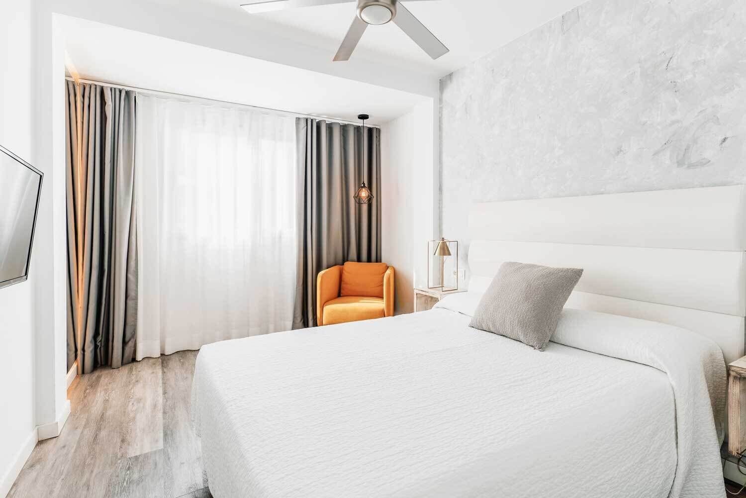 A modern hotel room with a large bed, a seating area with a chair, and a ceiling fan.