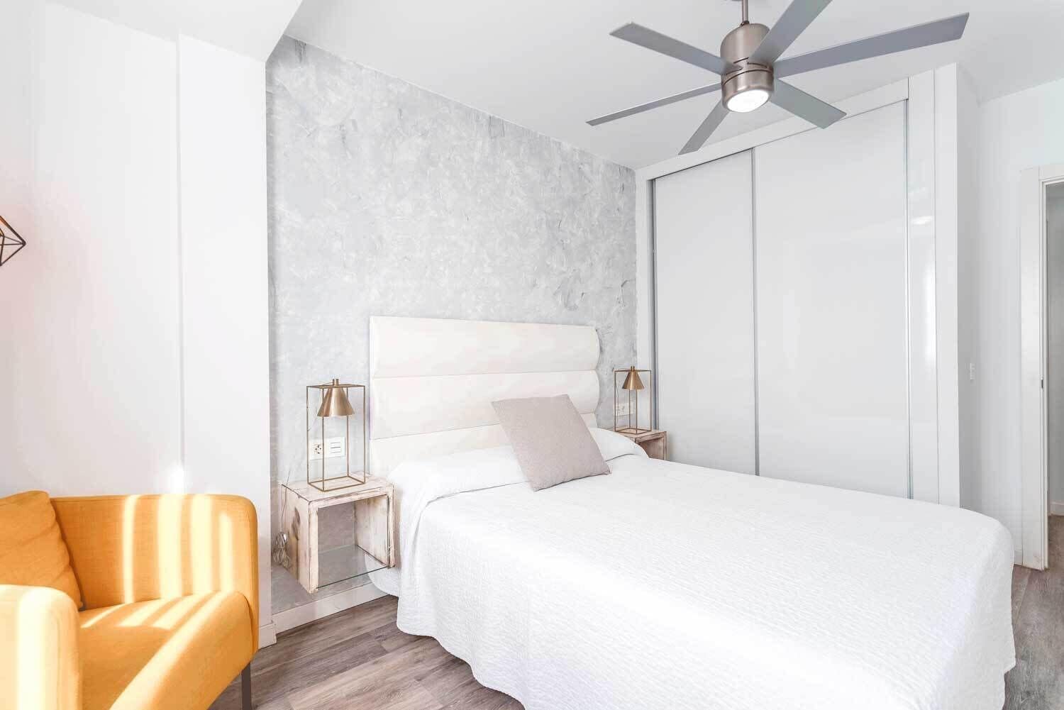 Un dormitorio moderno con una cama grande, un ventilador de techo y una mesita de noche con lámparas.