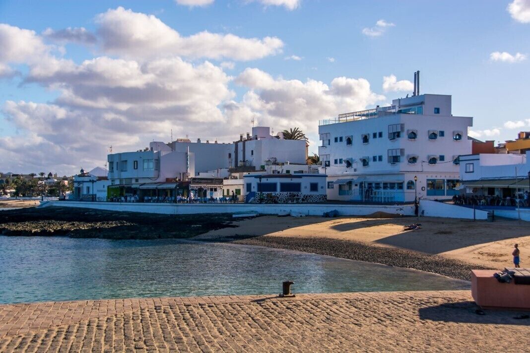 Een kustplaatsje met gebouwen aan de waterkant, een zandstrand en een heldere lucht.
