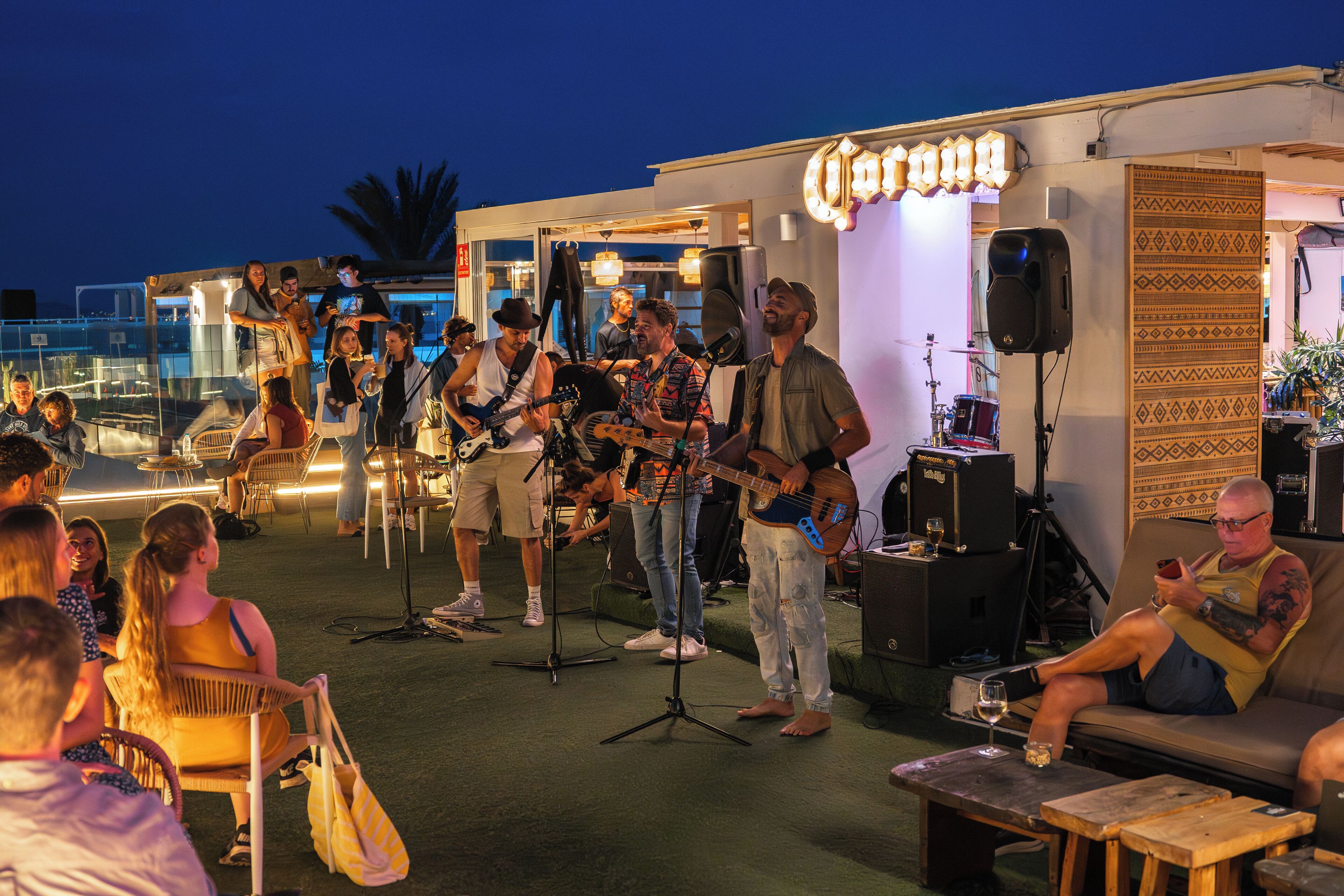 Evento serale all'aperto con una band che si esibisce su un palco, circondata da un pubblico seduto.