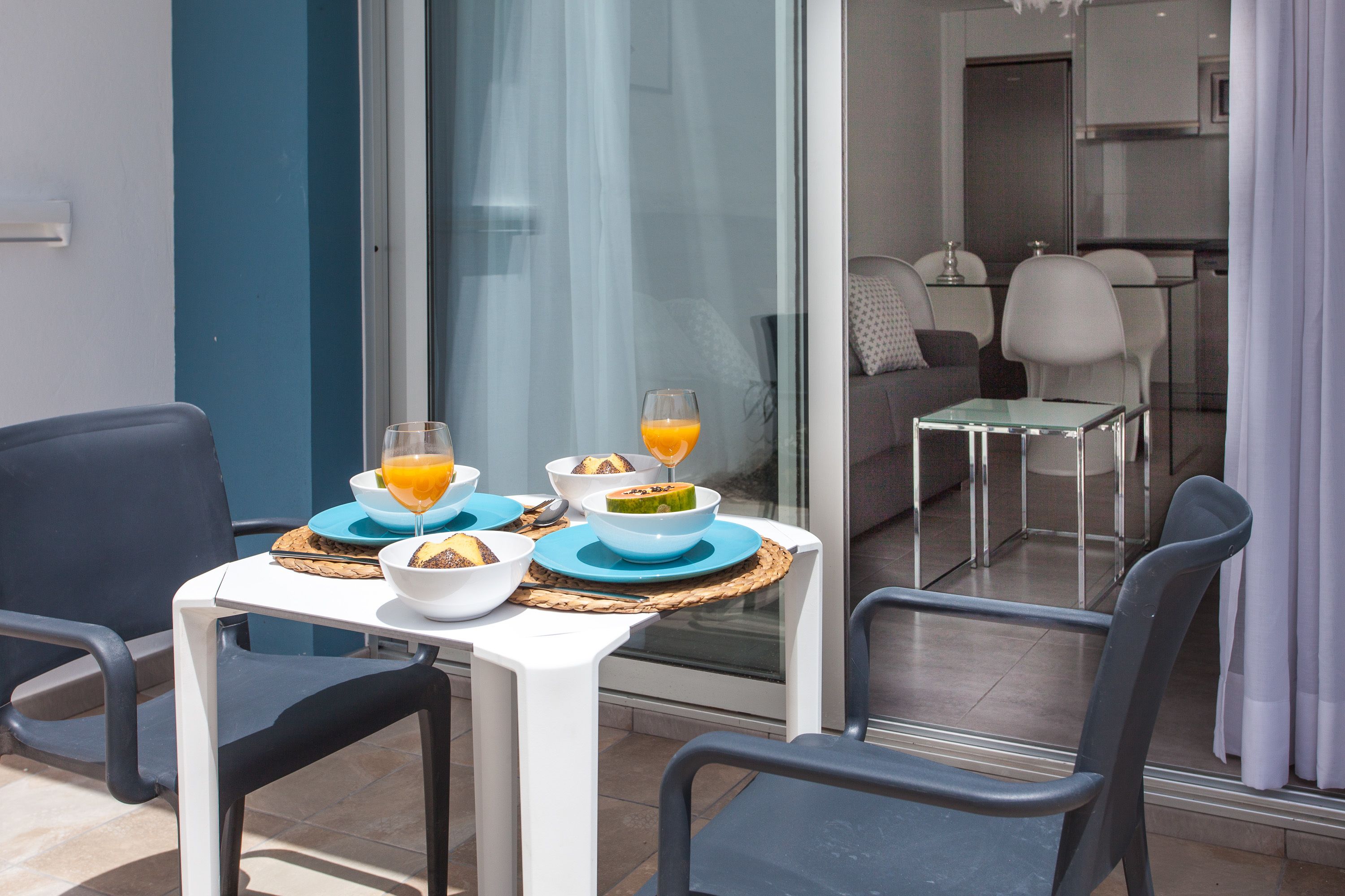 A dining area with a table set for two, featuring a glass partition, a sofa, and a kitchen in the background.