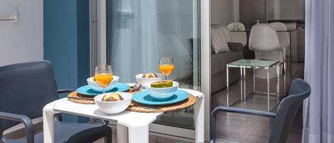 A dining area with a table set for two, featuring a glass partition, a sofa, and a kitchen in the background.