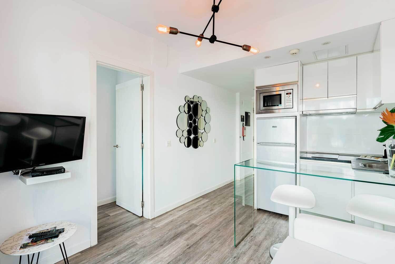 Una cocina moderna con gabinetes blancos, una mesa de comedor de vidrio y un microondas integrado.