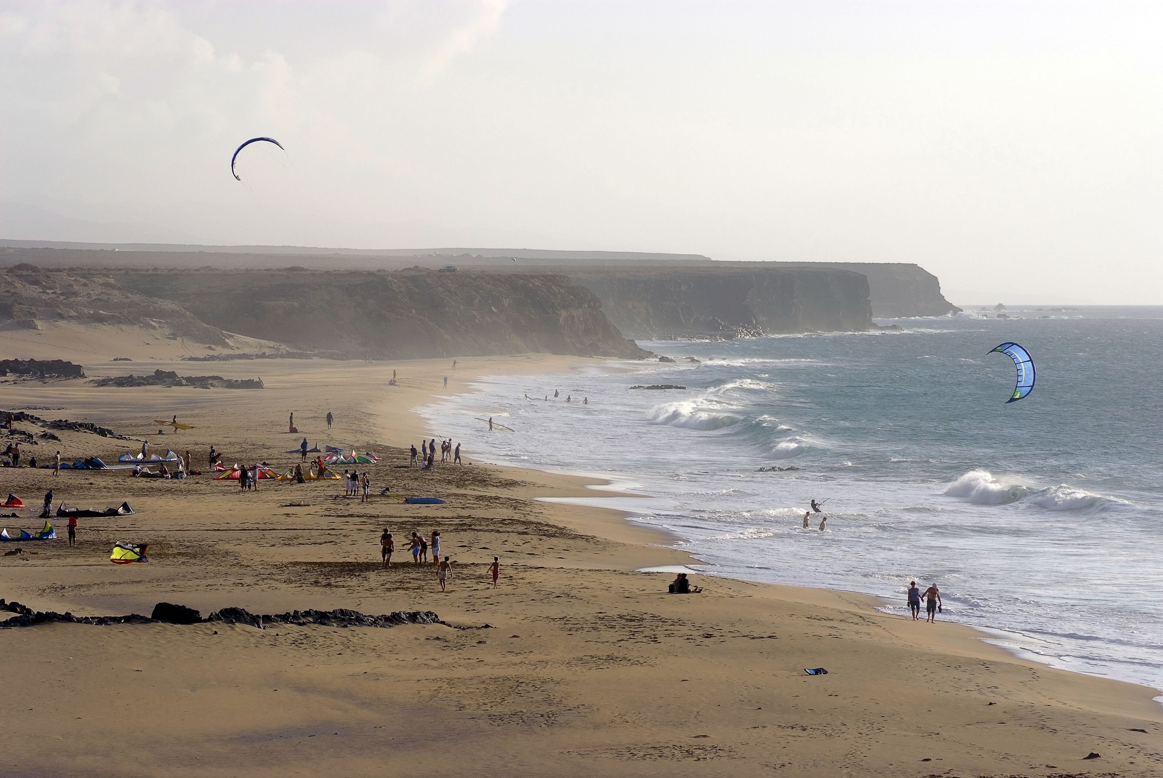 Une plage avec des tentes et des gens, des falaises en arrière-plan et un cerf-volant dans le ciel.