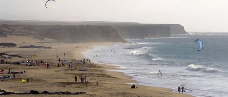 Une plage avec des tentes et des gens, des falaises en arrière-plan et un cerf-volant dans le ciel.
