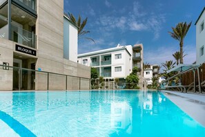Een zwembad met een helderblauw wateroppervlak, omgeven door moderne gebouwen met balkons en palmbomen.