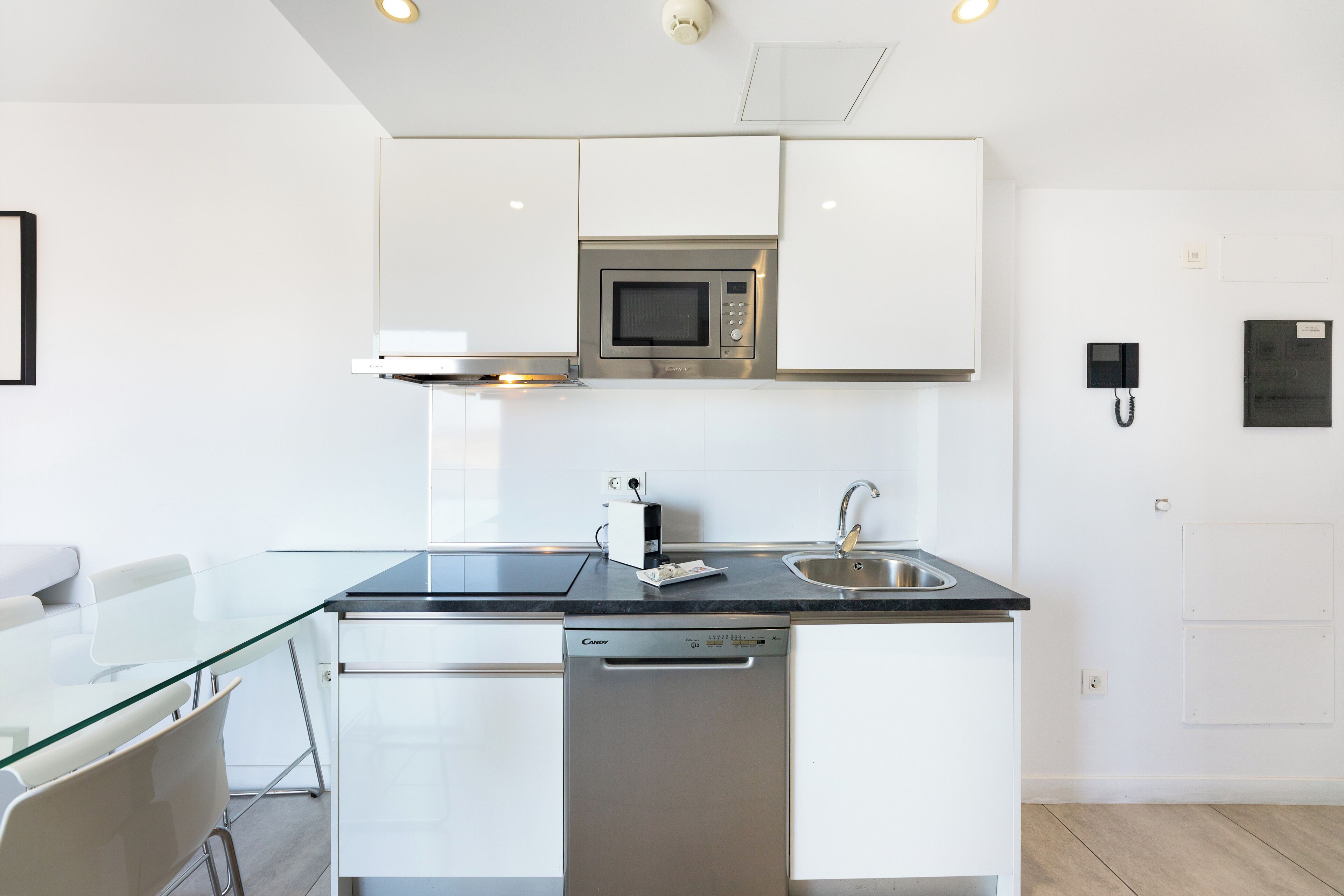 A modern kitchen with white cabinetry, a stainless steel microwave, a dishwasher, and a black countertop.