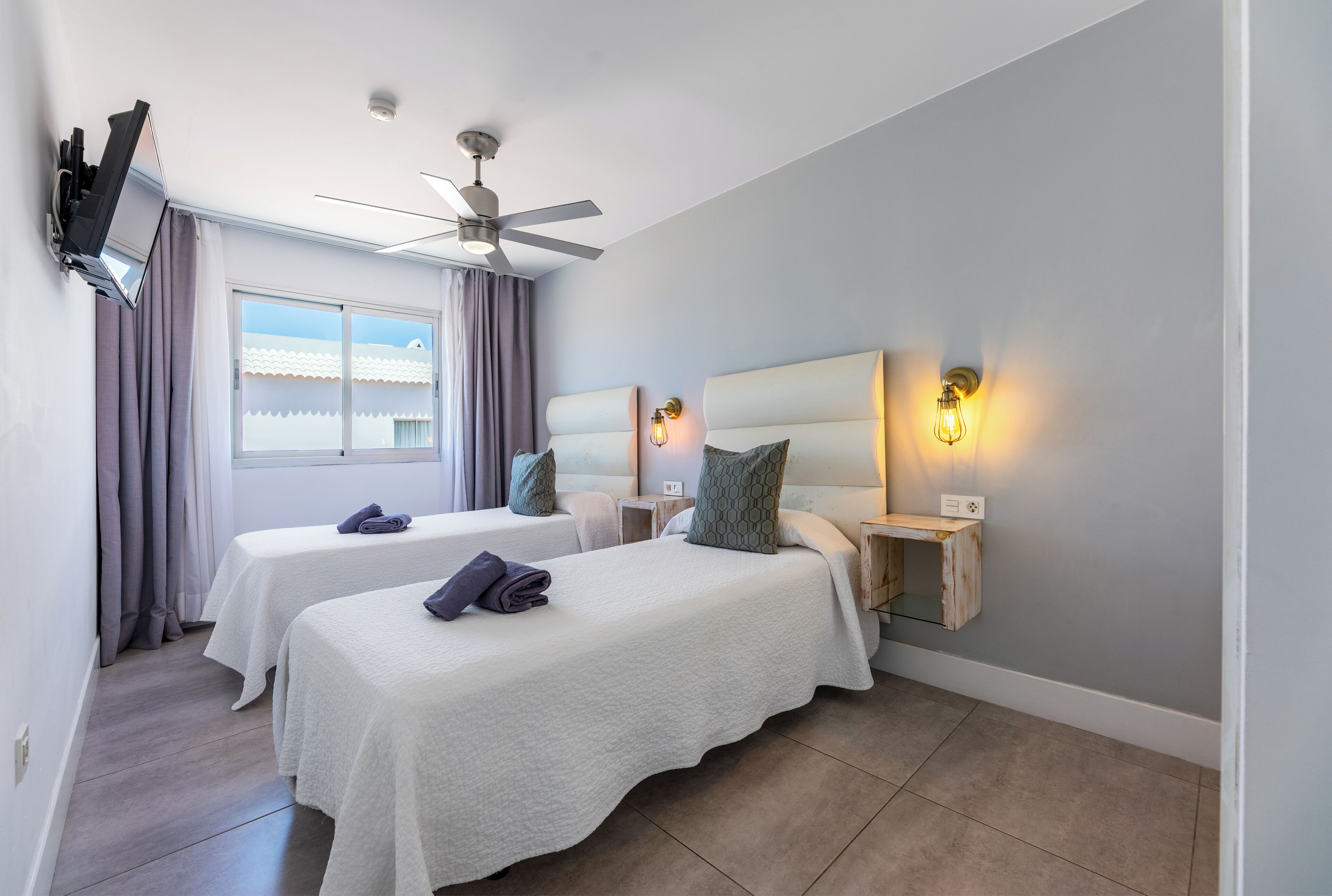 A hotel room with two beds, a ceiling fan, a window with curtains, and bedside lamps.