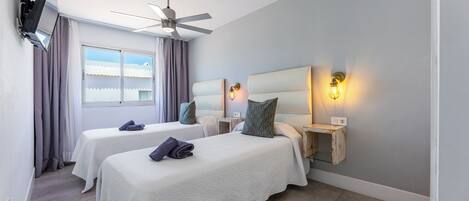 Ein Hotelzimmer mit zwei Betten, einem Deckenventilator, einem Fenster mit Vorhängen und Nachttischlampen.