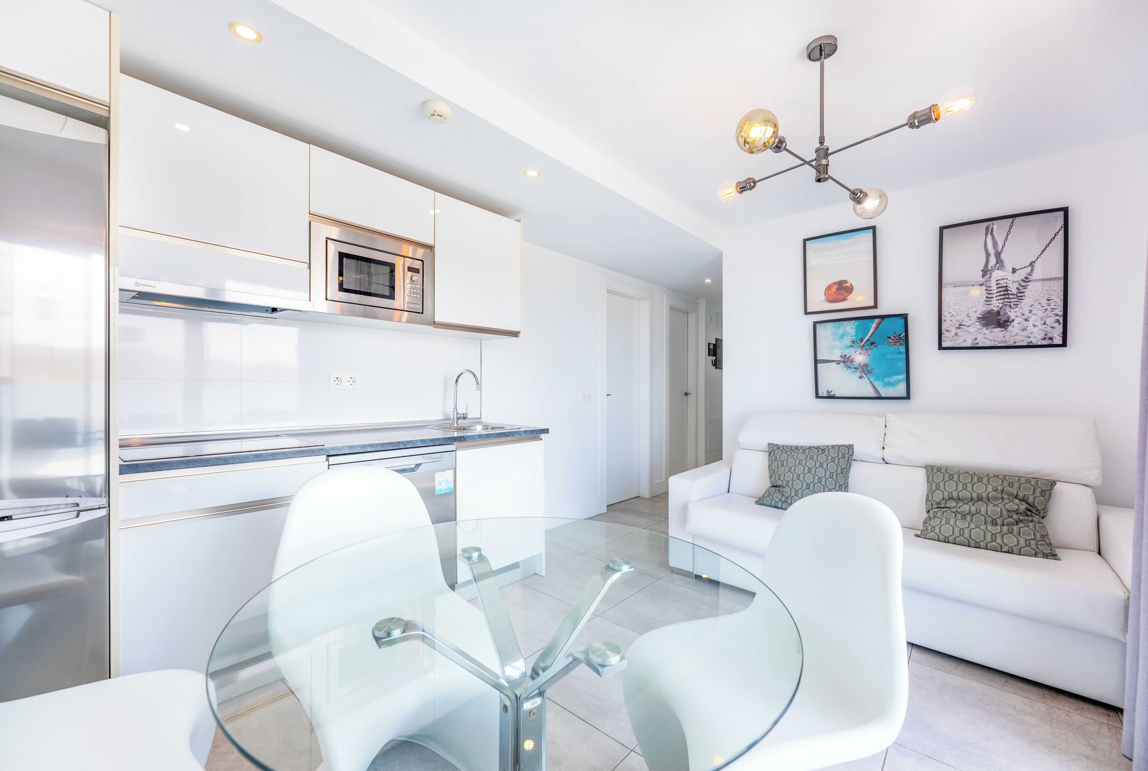 A modern kitchen with white cabinets, a built-in oven, and a glass dining table with chairs.
