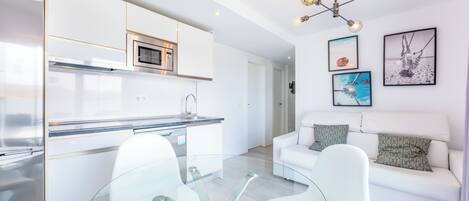 A modern kitchen with white cabinets, a built-in oven, and a glass dining table with chairs.