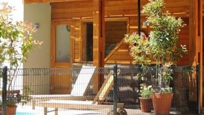 Un edificio de madera de dos pisos con balcones, plantas en macetas y un área exterior cercada.