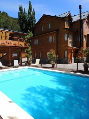 Un edificio de madera con piscina, sillas de descanso y plantas en macetas.