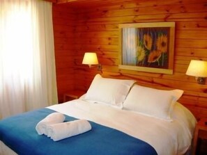 Una habitación tipo cabaña de madera con una cama, dos lámparas de noche y un cuadro en la pared.