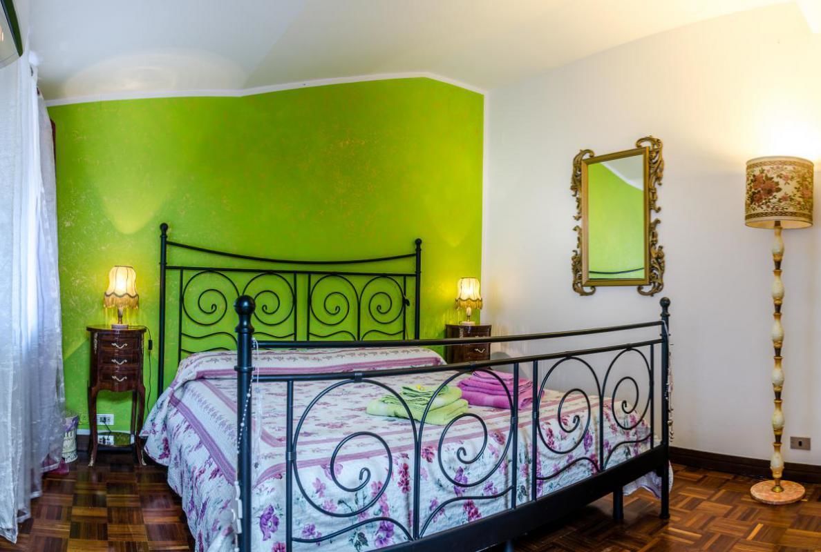 A room with a green accent wall, a metal bed frame, two bedside lamps, a mirror, and a floor lamp.