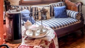 Ein gemütlicher Raum mit Holzboden, einer Couch mit gestreiften Kissen, einem Tisch mit Teekanne und Tassen sowie einem Fenster mit Vorhängen.