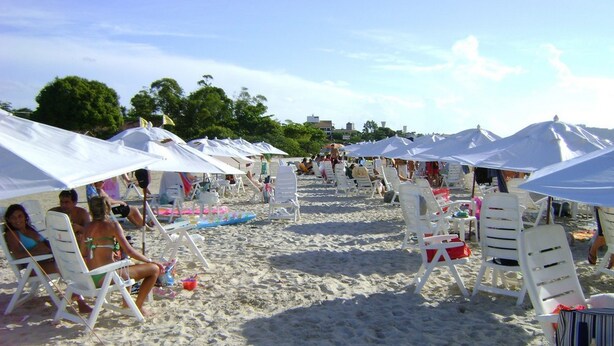 Una playa con hileras de sillas blancas bajo sombrillas blancas, dispuestas en línea.