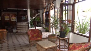 Un vestíbulo amplio con mobiliario de mimbre, piso de baldosas y plantas en macetas.