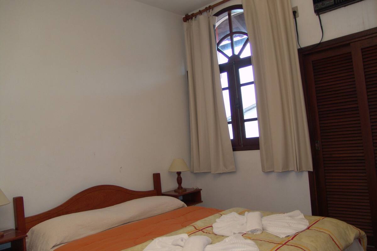 Un dormitorio con una cama individual, una mesita de noche, una lámpara y una ventana con cortinas.
