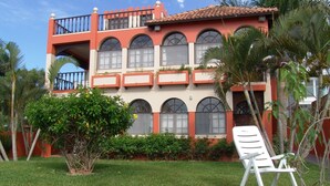 Un edificio de dos pisos con fachada roja y blanca, ventanas arqueadas grandes y un balcón con barandilla.
