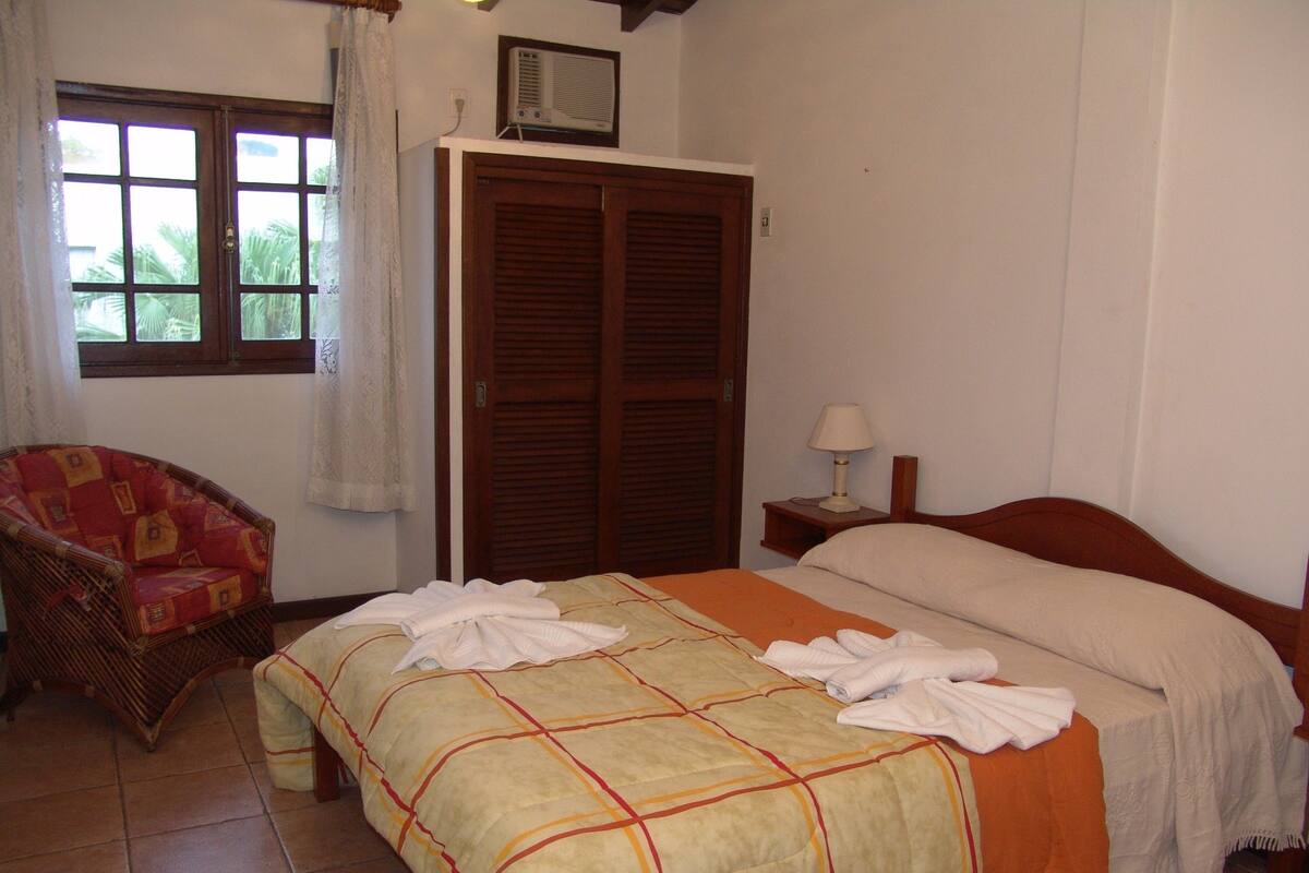 Un dormitorio con cama, una silla, un armario y una ventana.