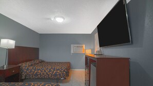 Habitación de hotel con dos camas, un escritorio, un televisor y una ventana con persianas.
