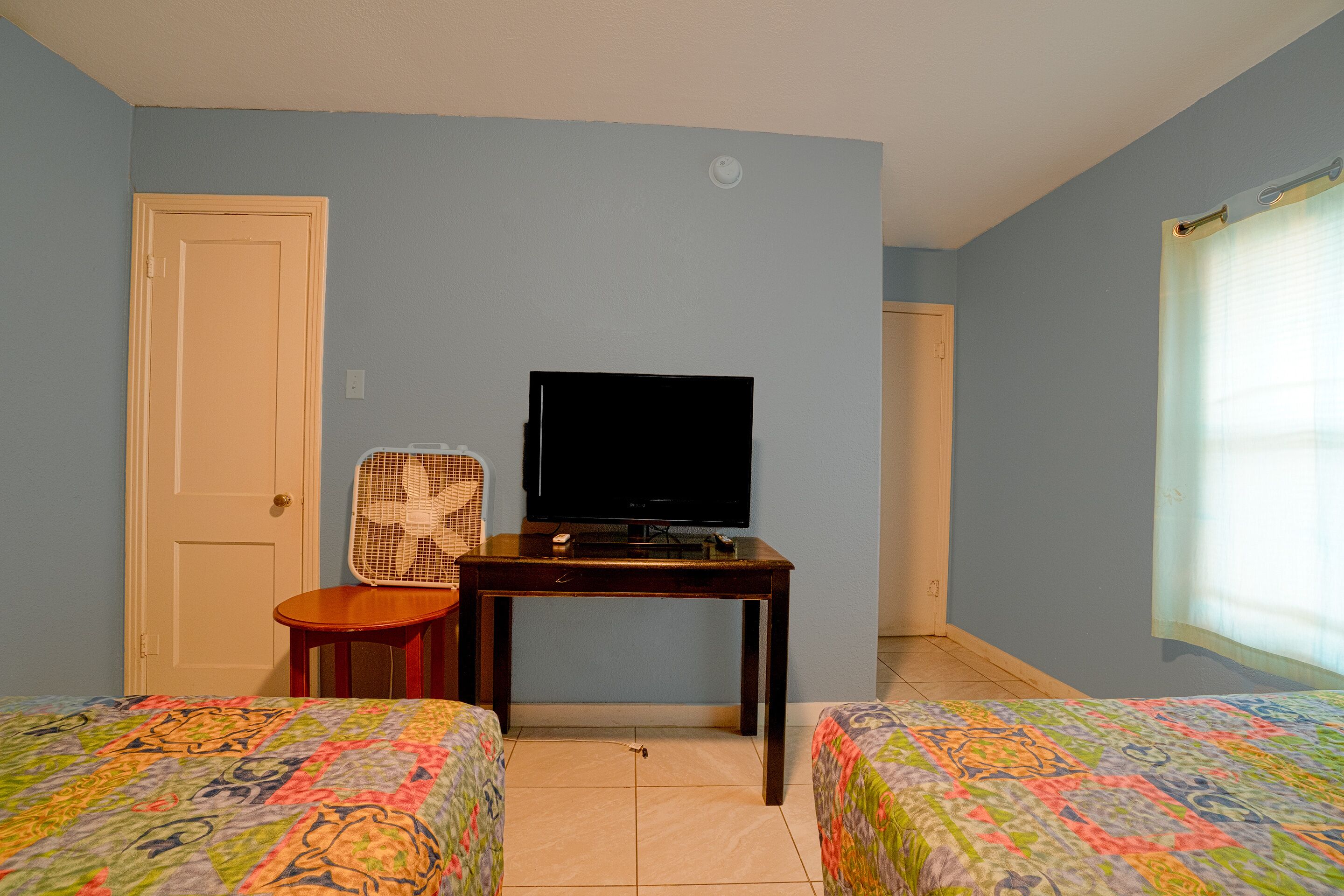 A room with two beds, a TV on a table, a chair, and a door.