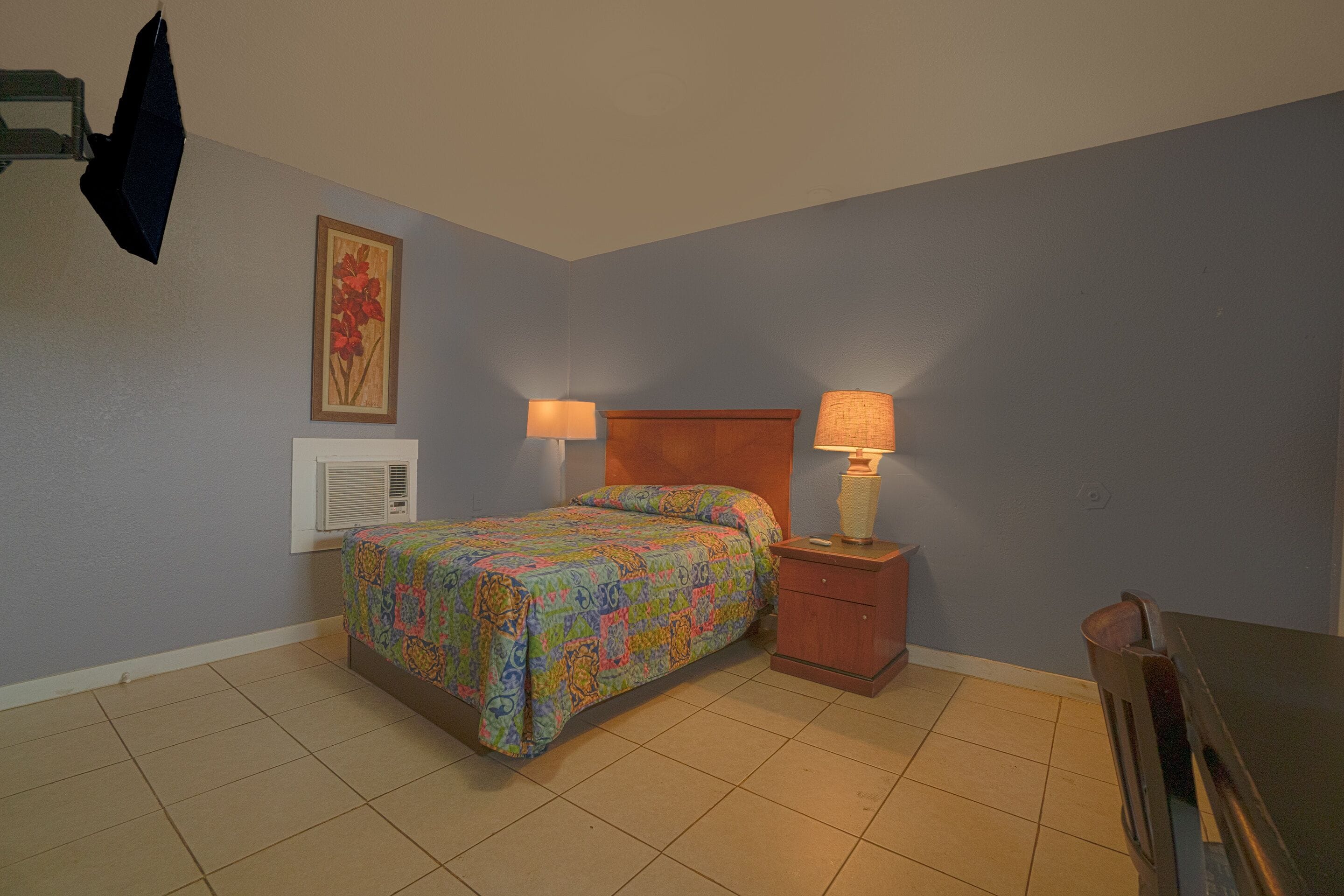 Une chambre à coucher avec un lit, des tables de chevet, une lampe, un radiateur et un tableau au mur.