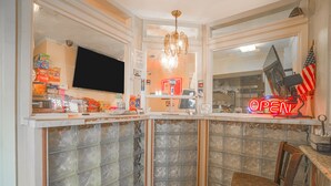 Rincón de bar con un letrero de neón que dice 'OPEN', una televisión y varios aperitivos y bebidas en estantes.