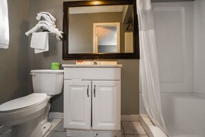 A bathroom with a toilet, a sink with a mirror above it, and a shower area.