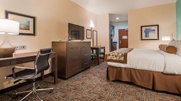 A hotel room with a desk, chair, bed, and a TV.