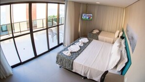 A hotel room with a large sliding glass door leading to a balcony, a bed with white linens, and a flat-screen TV mounted on the wall. - Acqua Suites (Maceió)