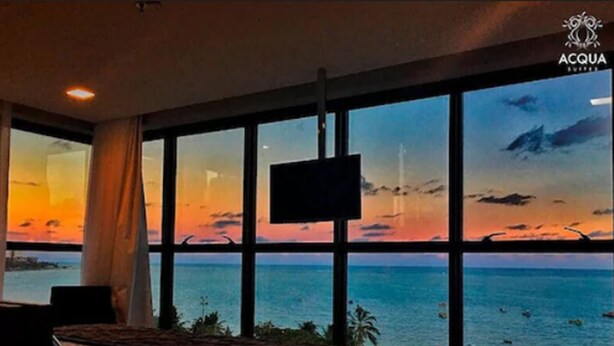 A hotel room with a large window offering a view of the ocean and a sunset. - Acqua Suites (Maceió)