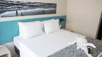 Una habitación de hotel con cama, almohadas blancas, una colcha, un cuadro en la pared, una mesita de noche y una lámpara.