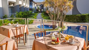 A poolside dining area with tables set for breakfast, overlooking a swimming pool and a landscaped garden. - Hotel Porto Nápolis (Eunapolis)