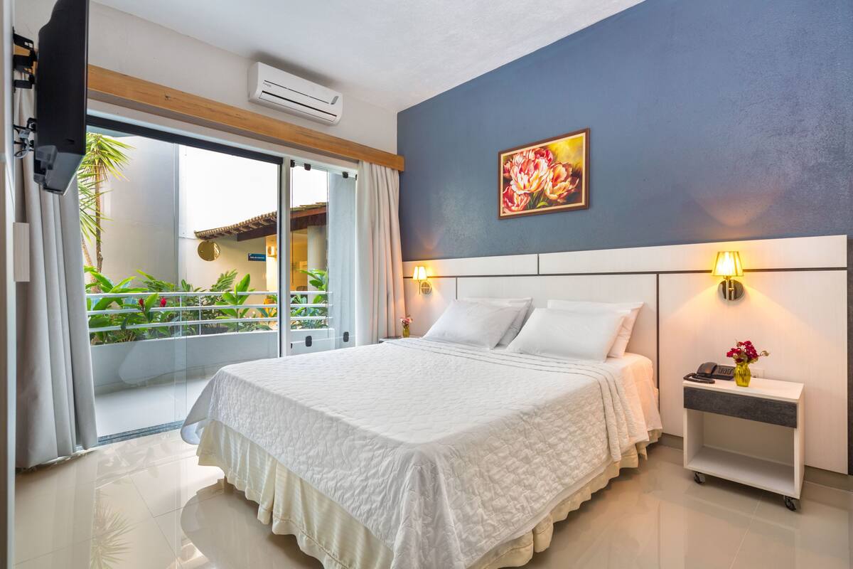 Un dormitorio con cama, mesita de noche, lámpara y un cuadro en la pared.