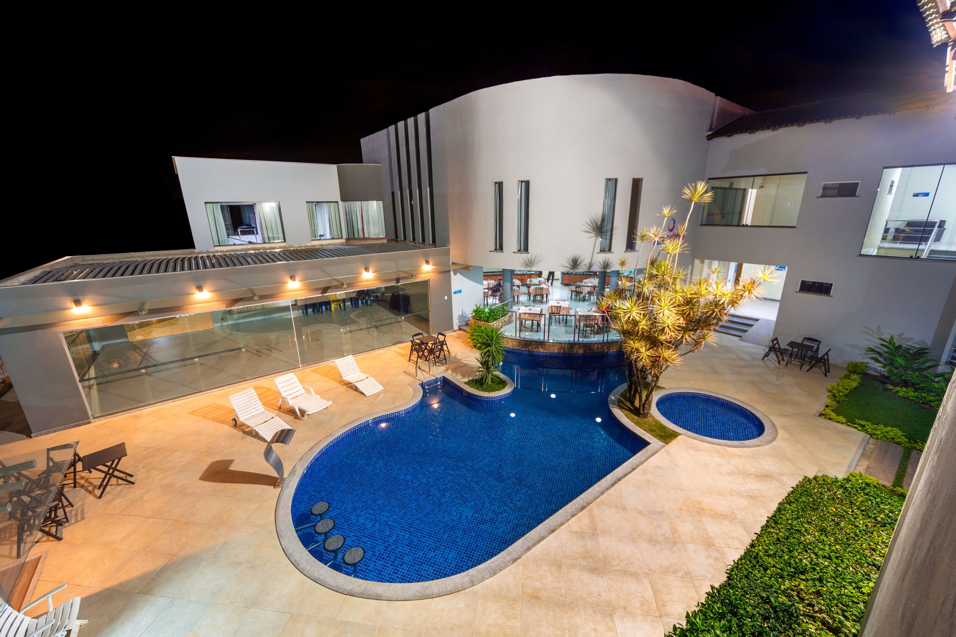 A modern hotel with a swimming pool, outdoor seating, and a well-lit terrace.